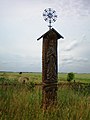 A roofed pole tipped with an ornate iron cross with floral motif. Angiras village, northwest of Josvainiai.