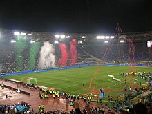 Football ground with floodlights, with green football pitch, streamers and confetti surrounded by a running track