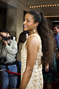 A woman wearing a tan/gold dress. She is looking toward the left, while smiling toward cameras.