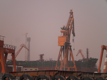 An unfinished ship and an orange crane at the center of an industrial setting