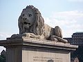 Wie ist der ungarische Name der Budapester Brücke deren Brückenköpfe von diesen Löwenstatuen bewacht werden?