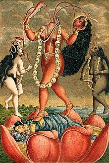 A decapitated, fair goddess stands on a copulating couple inside a large lotus. She holds her severed head and a scimitar. Three streams of blood from her neck feed her head and two nude (one white, another black coloured) women holding a knife and a skull-cup, who flank her. The goddess wears a skull-garland, a serpent (across her chest) and various gold ornaments.