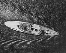 Overhead view of a large ship, much of which is covered with canvas sun shades, as it passes through calm waters.