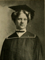A young woman facing the camera dressed in traditional college graduation cap and gown