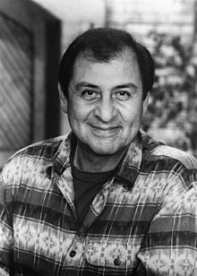 Handsome Latino man in his late sixties, smiling at the camera and wearing a striped shirt.