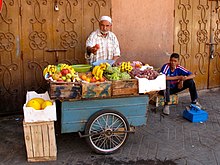 A man selling produce from a cart on the side of a street