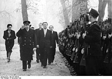 politicians walk in snow, past an honour guard with rifles