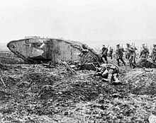 Group of armed soldiers marching past a wrecked tank and a body