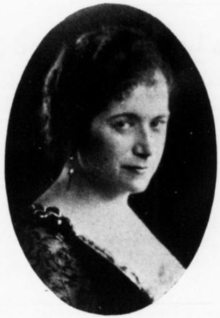 A white woman wearing a dark, lace-trimmed dress