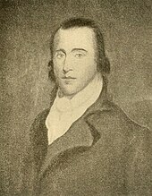 A man with long, receding black hair wearing a white, high-collared shirt and a black jacket