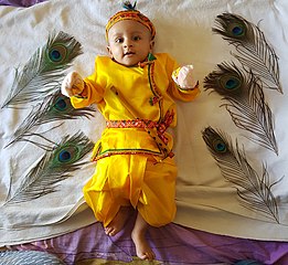 Indisches Kleinkind mit Krishnas Flöte, umgeben von sechs Pfauenfedern (2019)