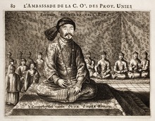 Black-and-white print of a man with small eyes and a thin mustache wearing a robe, a fur hat, and a necklace made with round beads, sitting cross-legged on a three-level platform covered with a rug. Behind him and much smaller are eight men (four on each side) sitting in the same position wearing robes and round caps, as well as four standing men with similar garb (on the left).