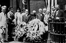 An audience in front of the plaque, behind a wreath of flowers.