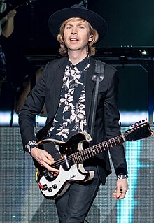 Beck onstage playing guitar and smiling, wearing a suit