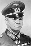 A man wearing a peaked cap, military uniform with an Iron Cross displayed at the front of his uniform collar.