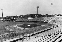 A black and white photograph of a baseball stadium in the final stages of construction, lacking infield dirt and warning track gravel