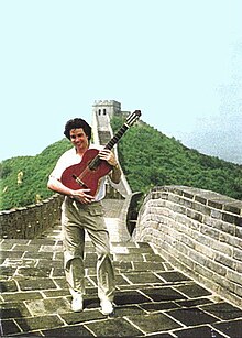 Laucke holding guitar and smiling, standing on top of the Great Wall of China