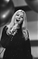 A black and white photo of a young blonde-haired woman holding a microphone and singing
