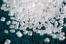Photograph showing crystals of refined sucrose. A millimetre ruler down the picture shows the scale of the grains is between 0.5 and 1 millimetre.