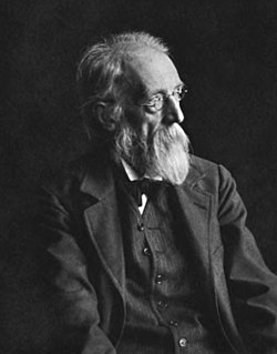 Photograph of a man in a three-piece suit with a beard and eyeglasses