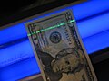 The security strip in a twenty-dollar bill glows green under a blacklight.