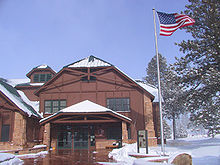 Two story wood building next to flag pole with U.S. flag waving in the wind. Snow on the ground.