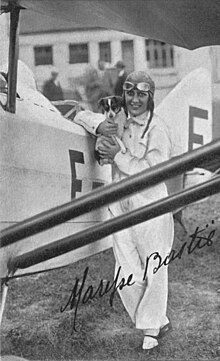 Maryse Bastié in her flying outfit of leather coat, cap and goggles, holding a large bunch of flowers - photo taken in 1932