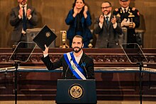 Nayib Bukele standing at a podium and holding up a legislative proposal in his right hand