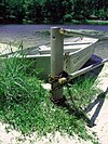 A metal rowboat chained to a metal pole with a lake behind