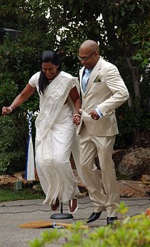 A Black couple hops over a broom at their wedding