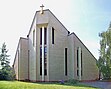 Das Bild zeigt ein modernes, in Dreiecksform aufragendes Kirchengebäude mit schmalen Fensterbändern. Auch der Grundriss ist dreieckig, die Farbe ein helles Gelb.