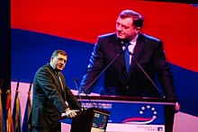 Milorad Dodik speaking at a podium and projected on a background screen