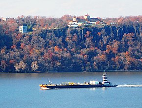 Panoramic view looking west from London Terrace. A barge on the Hudson River and the Hudson Palisades beyond, with the Englewood Cliffs campus of Saint Peter's University on the top of the Palisades