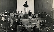 Charles de Gaulle speaking to a large group in a court-like room