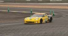 A photograph of a yellow and black grand touring racing vehicle exiting a racing circuit corner