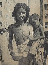A very shriveled and emaciated woman holding a very emaciated baby in the crook of her arm. Both are wearing only rags, and the mother's right breast is unconcealed. Her hands are holding a bowl and a canister, and she may be begging.