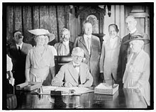 Thomas Marshall sitting at the Wilson desk surrounded by 8 people.