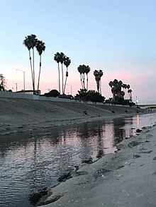 Concrete-paved banks of Ballona Creek channel, with palm trees silhouetted at sunrise