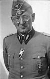 A man wearing a military uniform, side cap, and glasses.