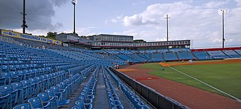 A view from the right-field line of the seating bowl at Greer. Blue seats stretch from the right-field wall, behind home plate, and beyond the third base dugout.