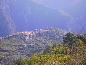 Photo looking down a town situated on a high plateau amid tree-covered mountains