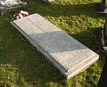 A granite headstone with a cross inscribed on it and a bunch of red and white flowers next to it, among many other gravestones