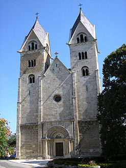The façade of a tall grey church with paired towers and a single ornately carved doorway