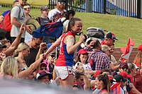Pearce standing on top of a fence and posing for a photo with her premiership medallion, with fans in the background