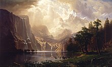 Painting of a lake with deer at the water's edge and the Sierra Nevada in the background. Light is shining between the clouds onto the mountains.