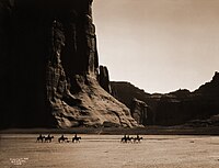 Canyon de Chelly – Navajo. Seven riders on horseback and dog trek against background of canyon cliffs, 1904