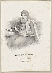 Turbaned man seated with a knife in his belt holding a peacock-feather fan