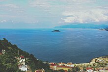 Photograph of the sea from a mountainous coastal city. The camera focuses on a wooded island.