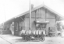 Norwalk, CA depot with deep eaves, loading docks and storefronts. A wagon, fully laden with milk cans is in front.