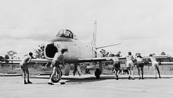 Black and white photograph of six men pushing a fighter jet on the ground